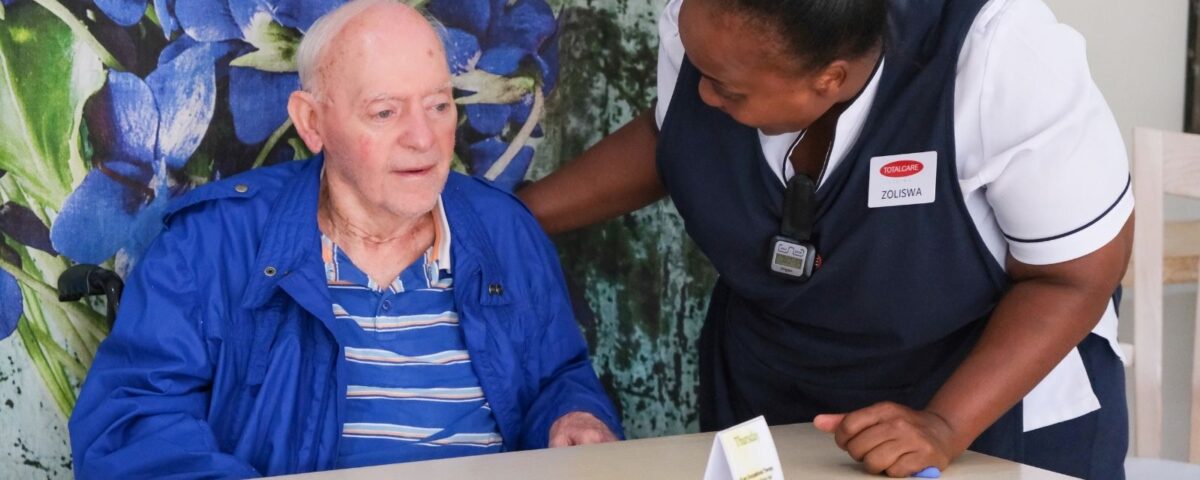 An older man seated beside a TOTALCARE care companion during an activity