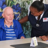 An older man seated beside a TOTALCARE care companion during an activity